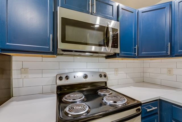 Kitchen with blue shaker cabinets, subway tile and stainless microwave